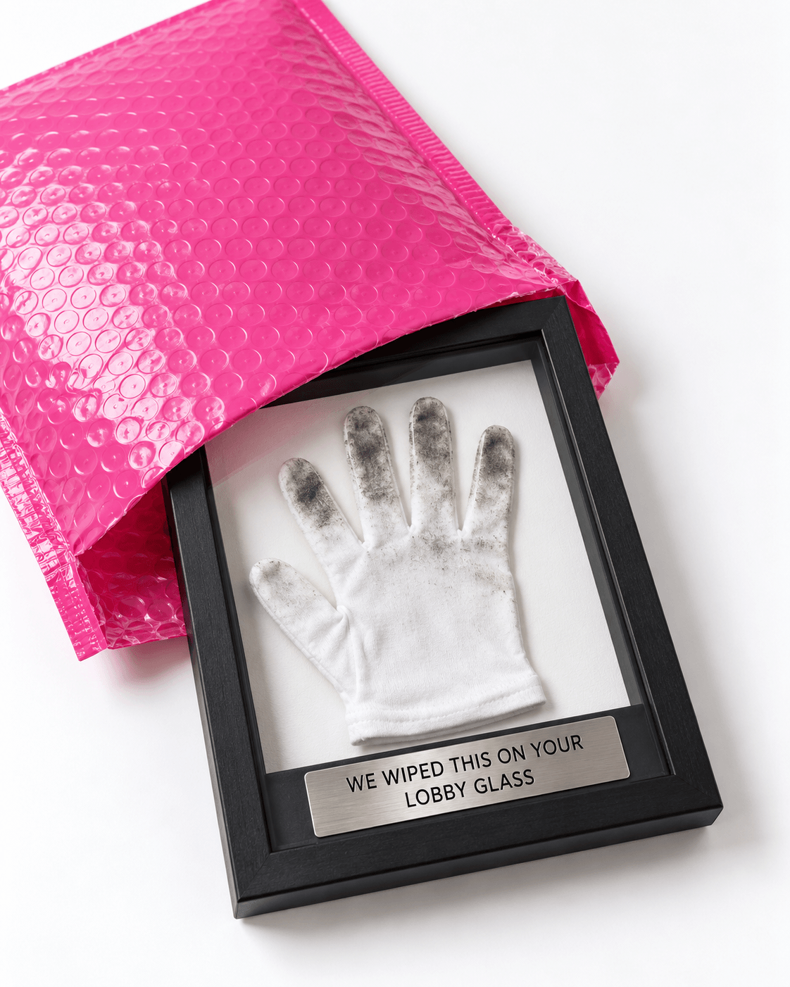 A pink bubble mailer with a framed white glove, dirty at the fingertips, under a plaque reading "We wiped this on your lobby glass."